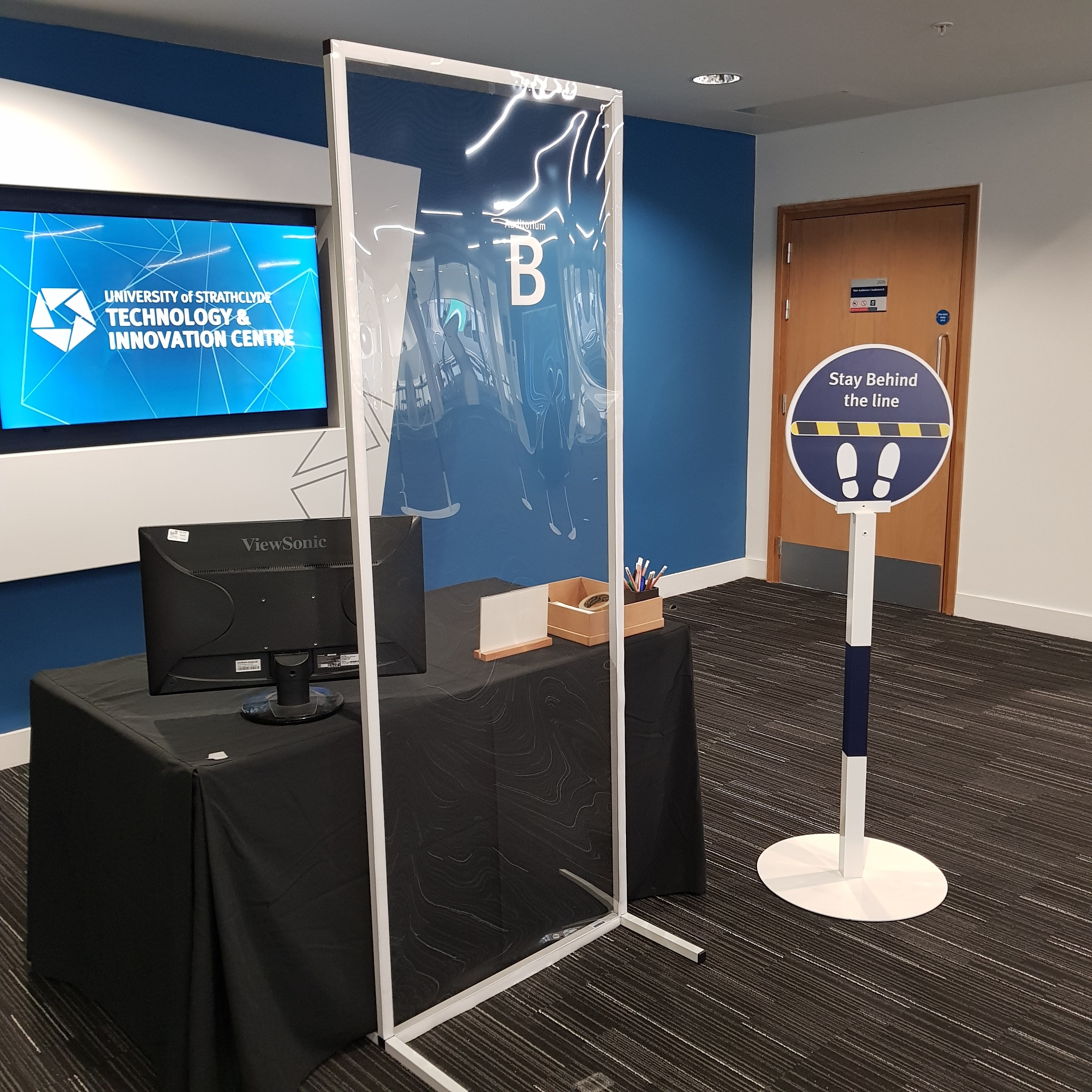 A conference organiser's desk in the Technology and Innovation Centre with safety screen and signage