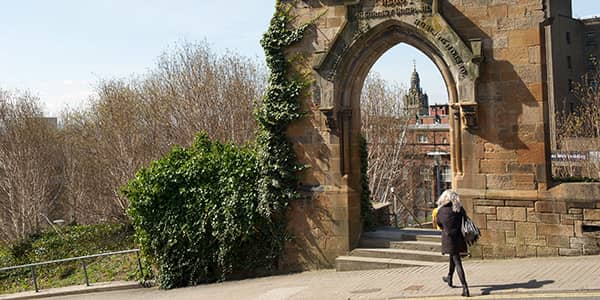 Student walking past archway at Rottenrow Gardens