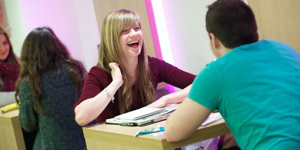 a female student laughs with another student over lunch in one of the campus cafes