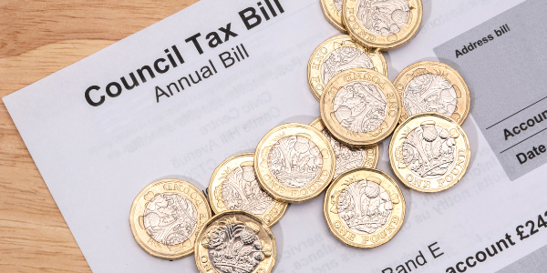 A printed council tax bill on a wooden table with a few pound coins laying on top.