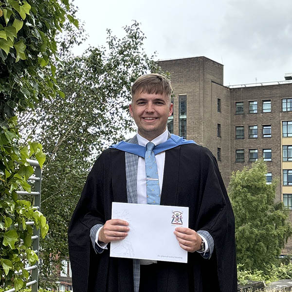 Jonathan Sneddon wearing graduation gown and holding degree certificate. Jonathan Sneddon wearing graduation gown and holding degree certificate.