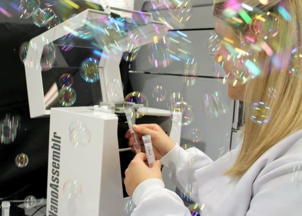 A researcher removes sample vials from a piece of lab equipment as bubbles float in the air