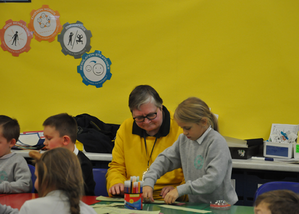 In a primary school classroom, a young girl does an activity while an older adult looks on