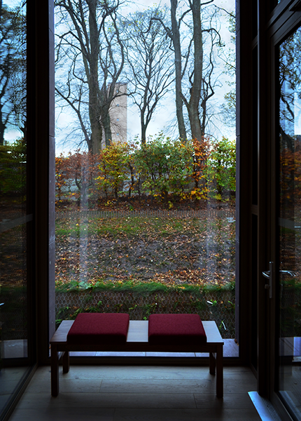 A bench in a building surrounded by windows looking out on gardens