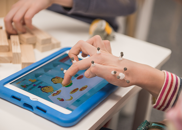 Close up of a child’s hand with sensors attached that track their movement as they play a game on a tablet