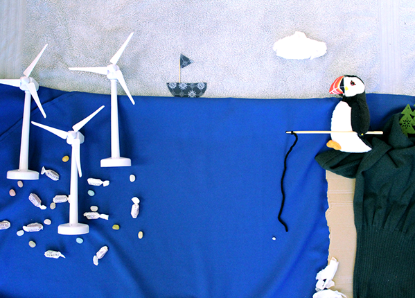A collage representing a puffin on a cliff edge with a fishing rod looking over to fish swimming beneath offshore wind turbines A collage representing a puffin on a cliff edge with a fishing rod looking over to fish swimming beneath offshore wind turbines
