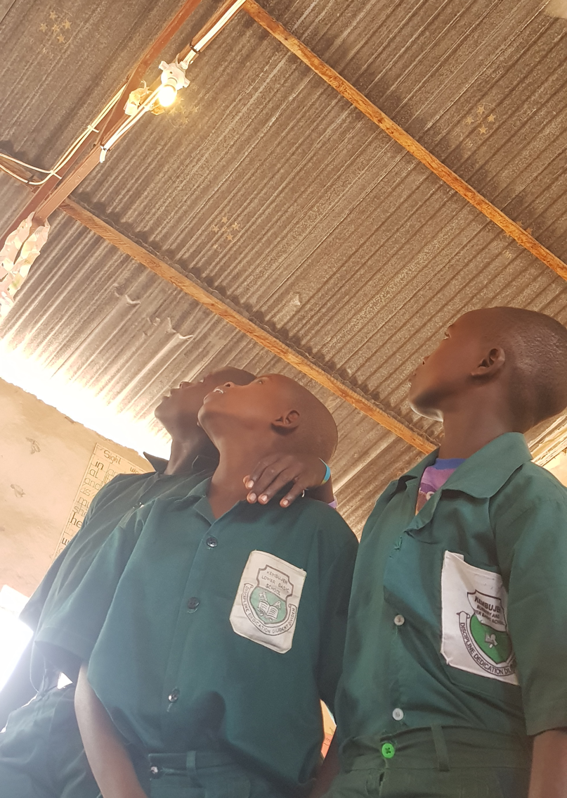 Three young African boys look up to a lightbulb in the ceiling