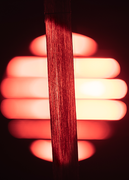 A very thin strand of a novel material in front of a large red light