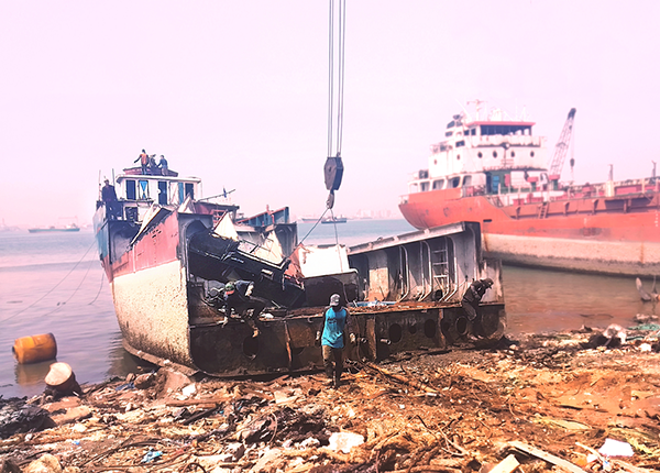 An old ship being dismantled on the shore surrounded by debris