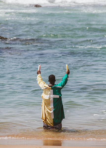 An African man standing in the sea, holding candles in the air, performing a religious ritual