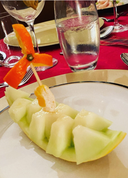 A boat and wind turbine sculpted from fruit, on a plate in a restaurant
