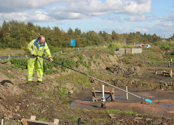 A man in high-viz clothing raking a former canal site