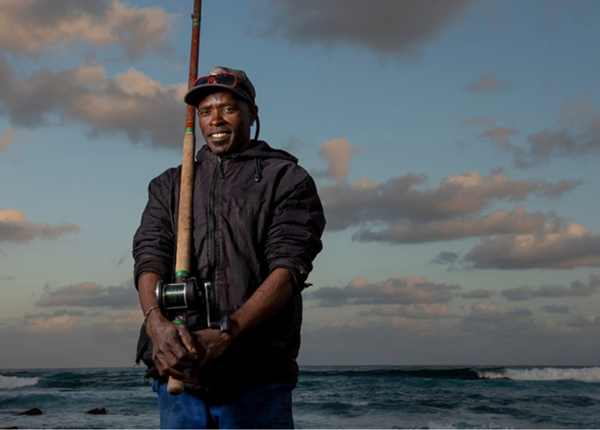 An African small scale fisherman with fishing rod standing in front of the sea