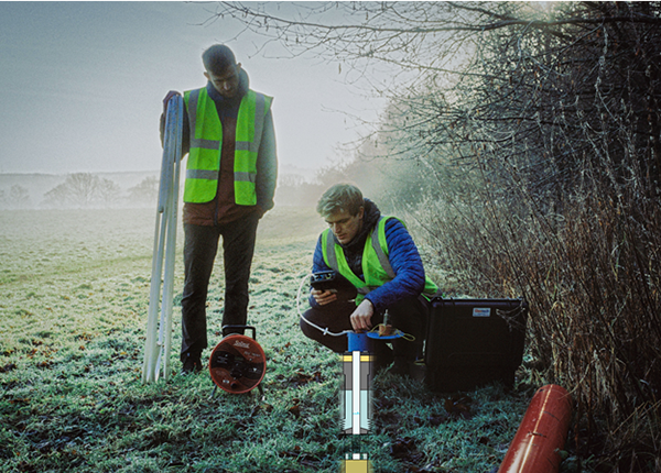 A researcher crouching on the grass testing the ground with a researcher standing watching