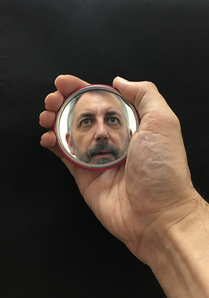 A hand holding a small mirror with the reflection of a man in it