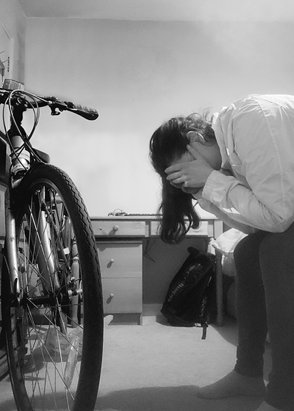 A woman sits on a bed with her head in her hands and a bike in front of her