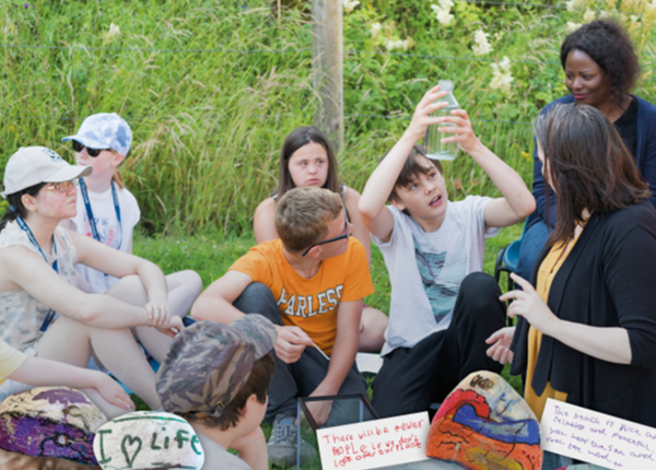 Group of young people sitting on grass with teachers while one holds up a bottle looking into it