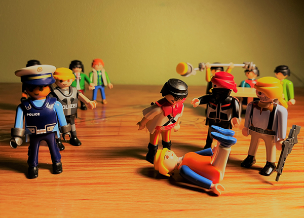 A victim on the ground surrounded by perpetrators and authorities, portrayed by Playmobil figures 