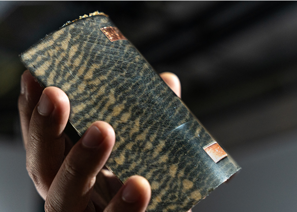 A close up of a hand holding a curved patterned board with two copper rectangles