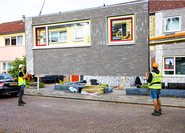 Two workmen controlling the placement of an exterior panel onto the front of a house