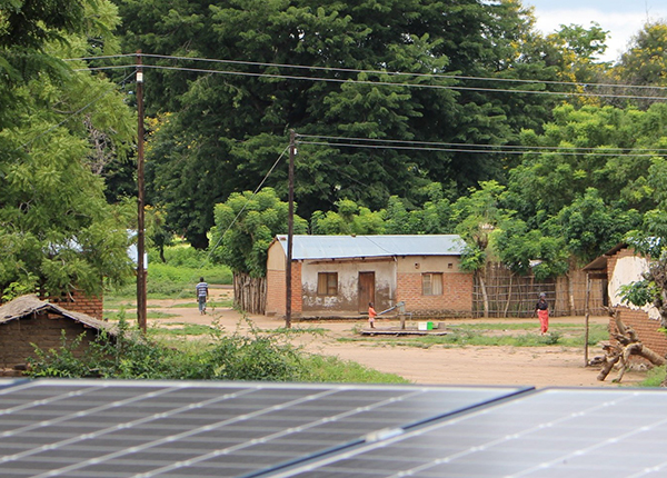 Solar panels in the foreground, small buildings with rooftop solar panels in the background, in Malawi     