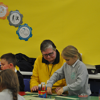 In a primary school classroom, a young girl does an activity while an older adult looks on