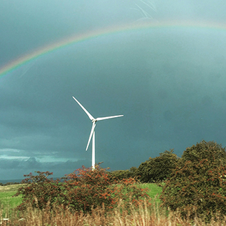 : A single wind turbine on a hillside with a rainbow arching over it