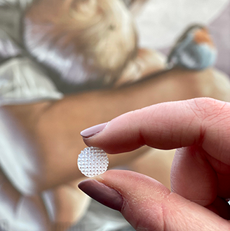 Close up of a hand holding a tablet with a textured surface in front of a painting on a wall depicting a mother breast feeding her child