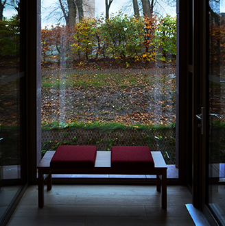 A bench in a building surrounded by windows looking out on gardens