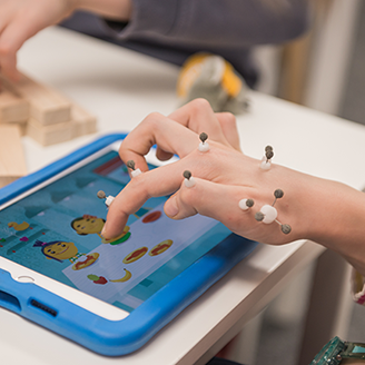 Close up of a child’s hand with sensors attached that track their movement as they play a game on a tablet