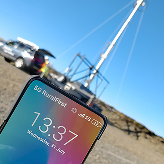 A hand holding a mobile phone in front of a phone mast in a remote location