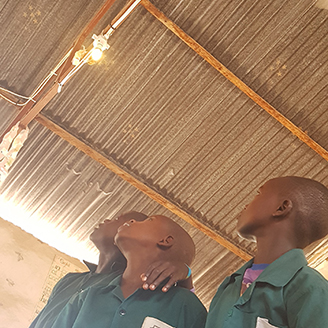 Three young African boys look up to a lightbulb in the ceiling