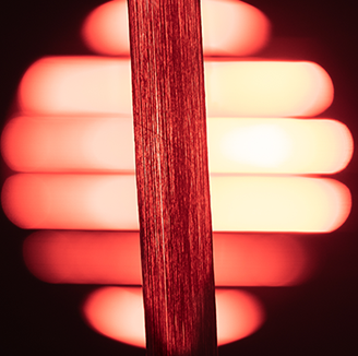 A very thin strand of a novel material in front of a large red light