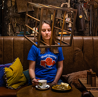 A young woman sits in a café booth with her head in a wooden cage 