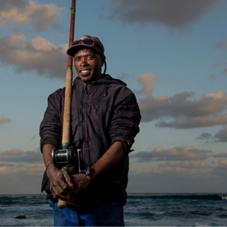 An African small scale fisherman with fishing rod standing in front of the sea