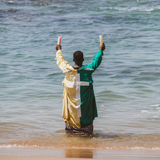 An African man standing in the sea, holding candles in the air, performing a religious ritual