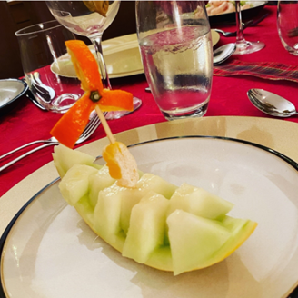 A boat and wind turbine sculpted from fruit, on a plate in a restaurant