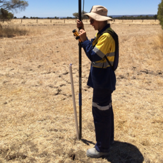 A female researcher standing in a dried out field with a measurement device
