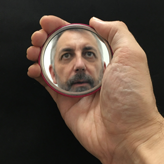 A hand holding a small mirror with the reflection of a man in it