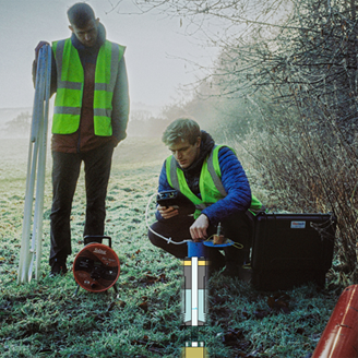 A researcher crouching on the grass testing the ground with a researcher standing watching