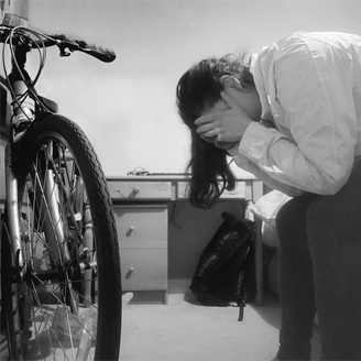 A woman sits on a bed with her head in her hands and a bike in front of her