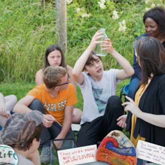 Group of young people sitting on grass with teachers while one holds up a bottle looking into it