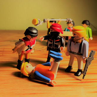 A victim on the ground surrounded by perpetrators and authorities, portrayed by Playmobil figures 