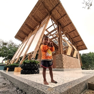 A child stands in front of a bamboo building