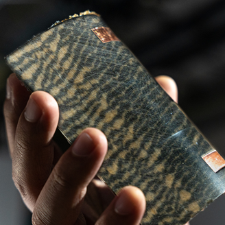 A close up of a hand holding a curved patterned board with two copper rectangles 