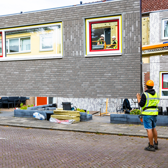 Two workmen controlling the placement of an exterior panel onto the front of a house