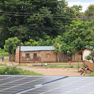Solar panels in the foreground, small buildings with rooftop solar panels in the background, in Malawi  