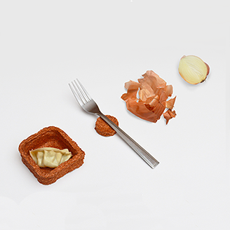 A slice of onion next to crumpled onion skins, a fork next to a little rough-textured container holding a gyoza