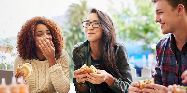 two women and a man eat burgers and laugh