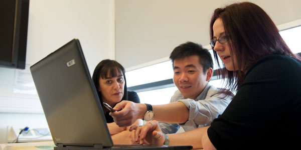 three people looking at a laptop screen and having a conversation